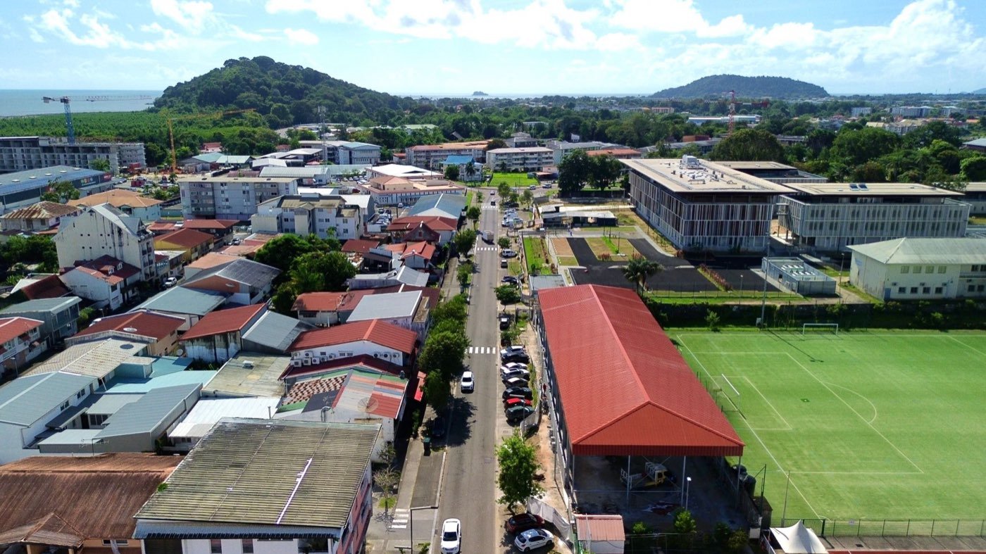 Vue aérienne d'une rue de Cayenne entre maisons, immeubles et équipements sportifs